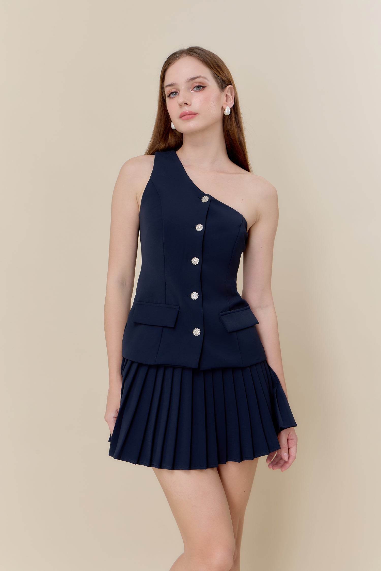 Woman wearing a navy one-shoulder dress with buttons on a beige background