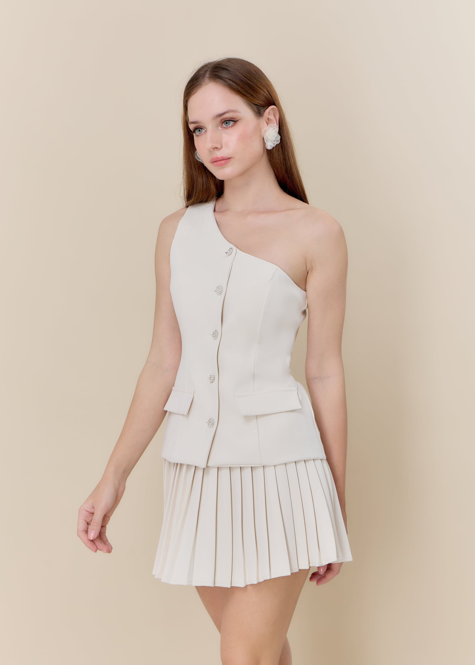 Woman wearing a one-shoulder beige dress with a pleated skirt on a beige background