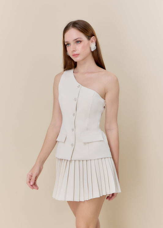 Woman wearing a one-shoulder beige dress with a pleated skirt on a beige background